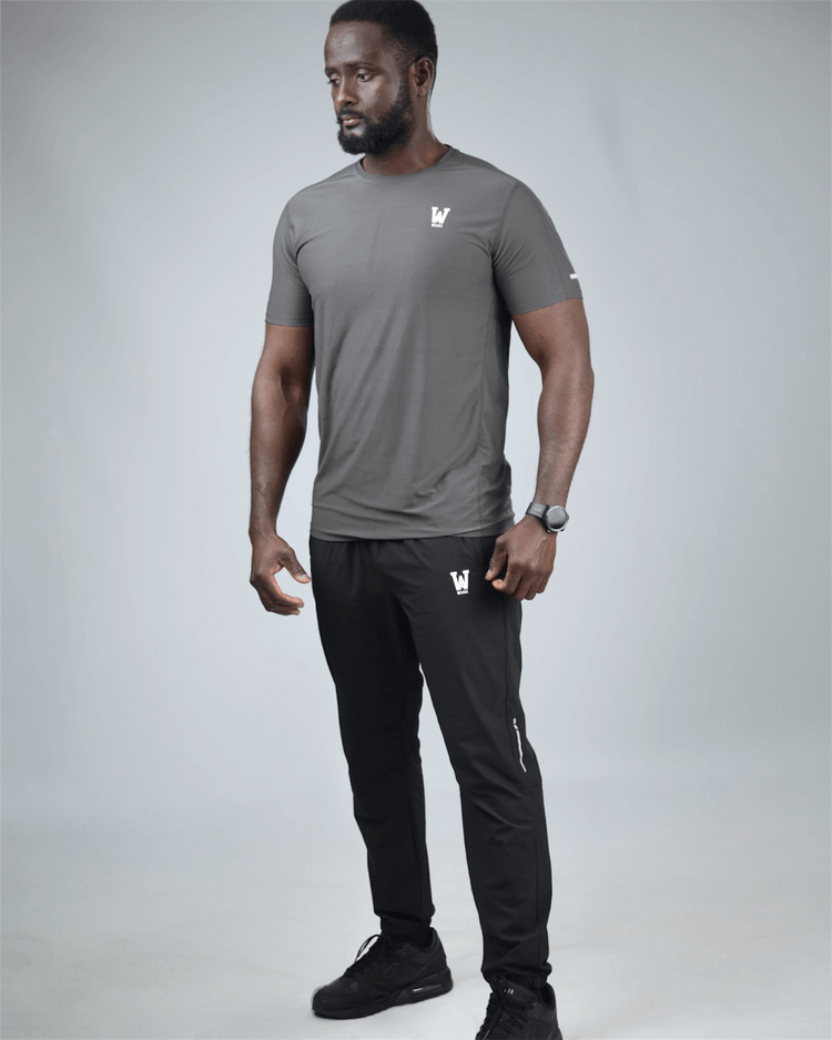 Man wearing a gray t-shirt and black pants with logos on a light gray background