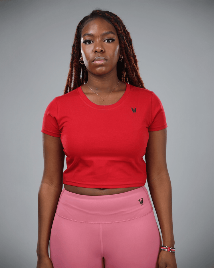 woman wearing a red crop top and pink leggings with waaka logo on a grey background front view