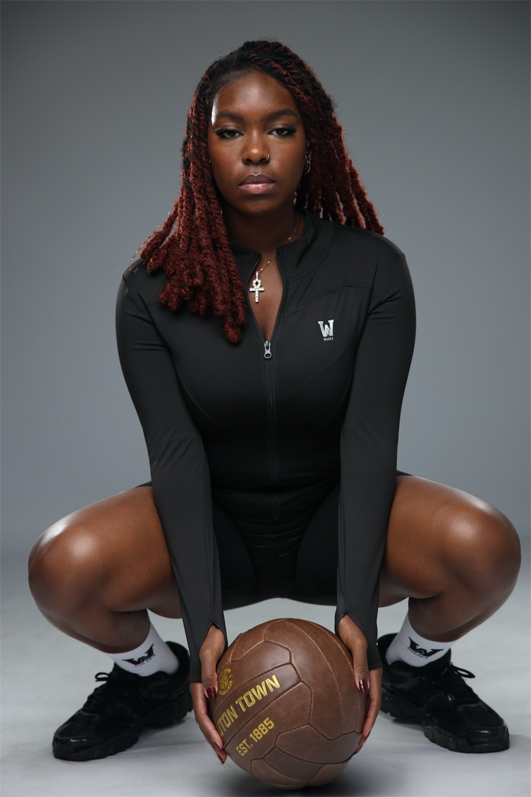 Woman in black athletic outfit holding a basketball on a gray background
