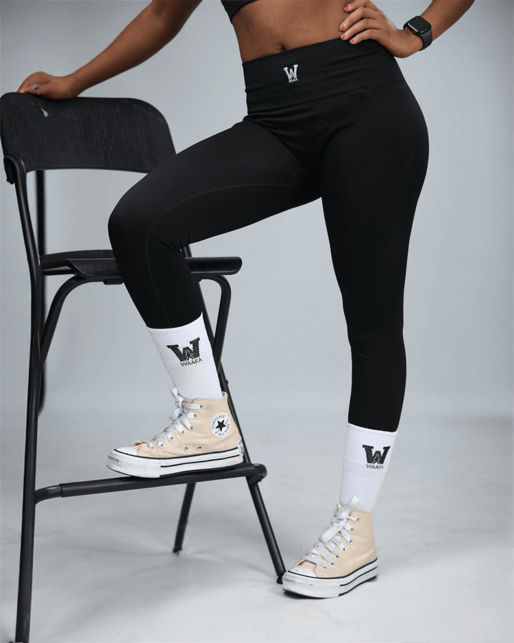 Person wearing black leggings with waaka logo, standing on a chair against a plain background