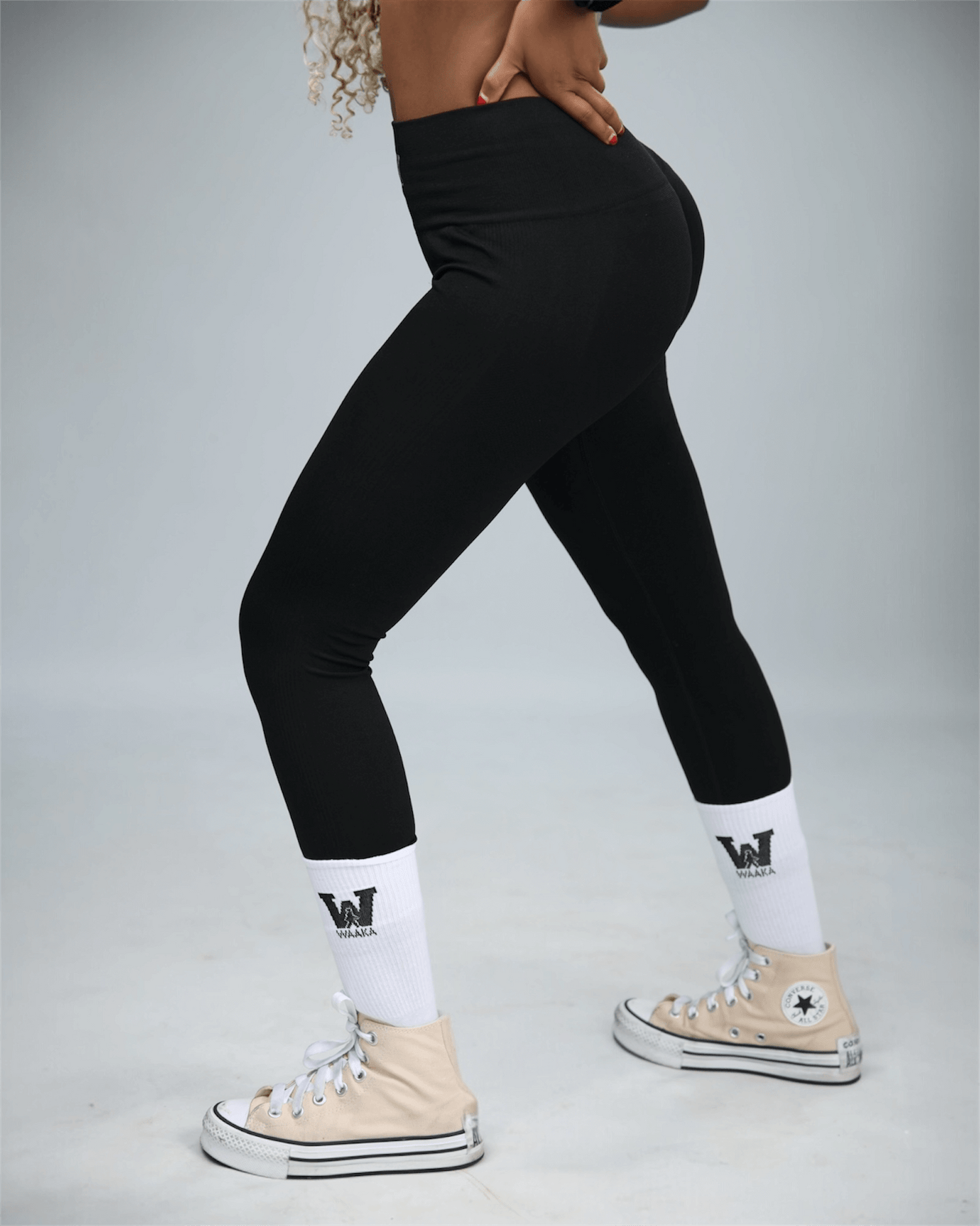 woman wearing black leggings and beige Converse shoes on a grey background