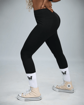 woman wearing black leggings and beige Converse shoes on a grey background