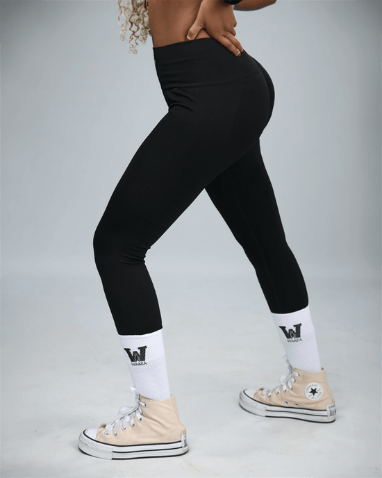 woman wearing black leggings and beige Converse shoes on a grey background