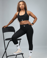 Woman in black waaka athletic wear posing on a chair against a gray background