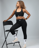 Woman in black athletic wear posing on a chair against a gray background