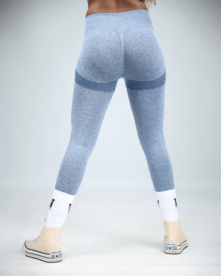 Person wearing blue leggings with white socks and sneakers on a light gray background back view