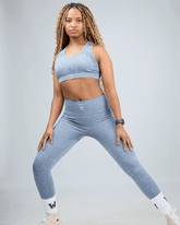 Woman wearing a gray sports bra and leggings set on a light gray background