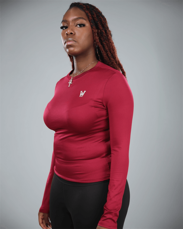 Woman wearing a red long-sleeve shirt with waaka logo on a gray background side view