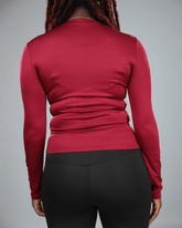 Person wearing a red long-sleeve top and black pants on a gray  background back view