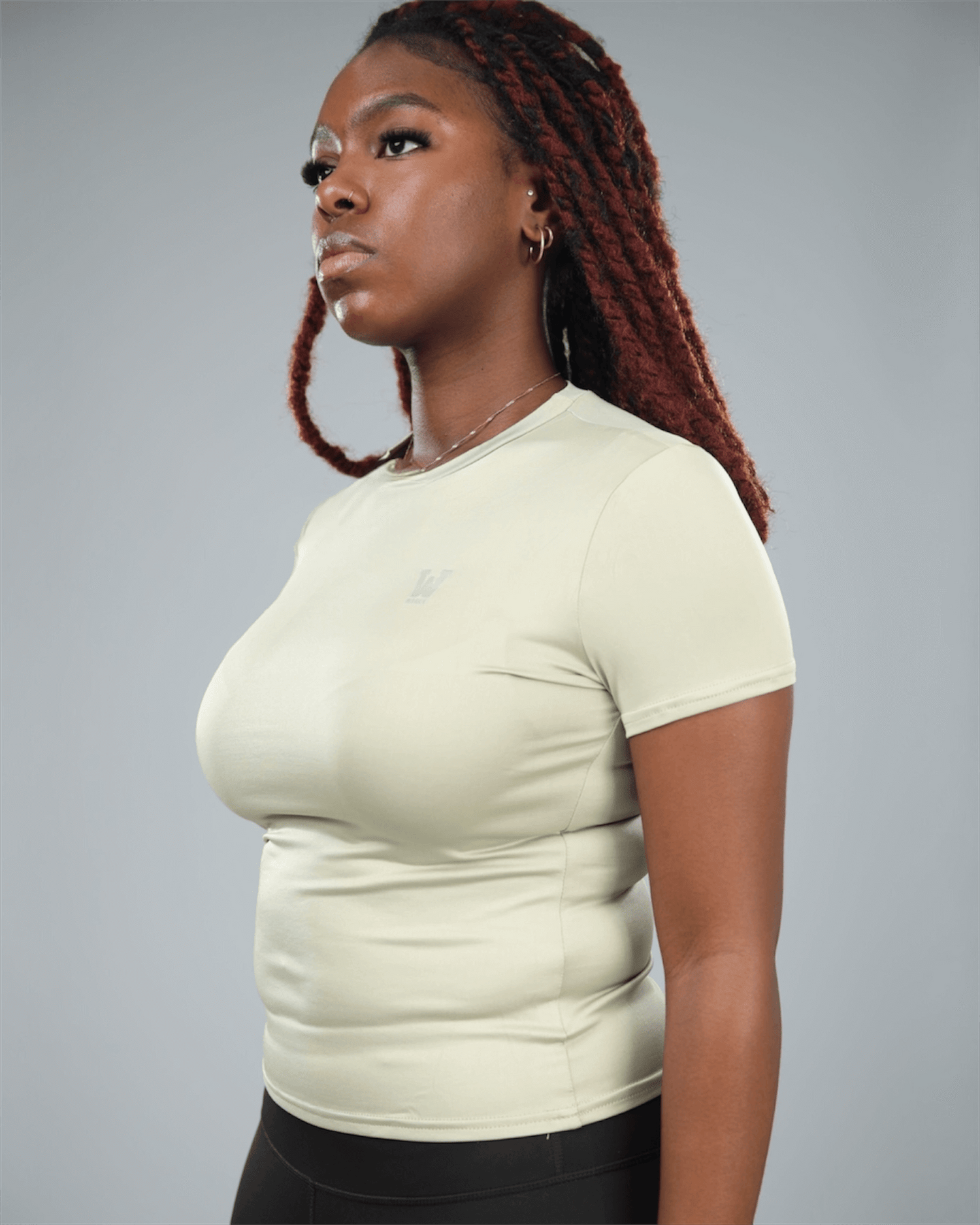 Woman wearing an olive green t-shirt and black leggings against a grey background side view