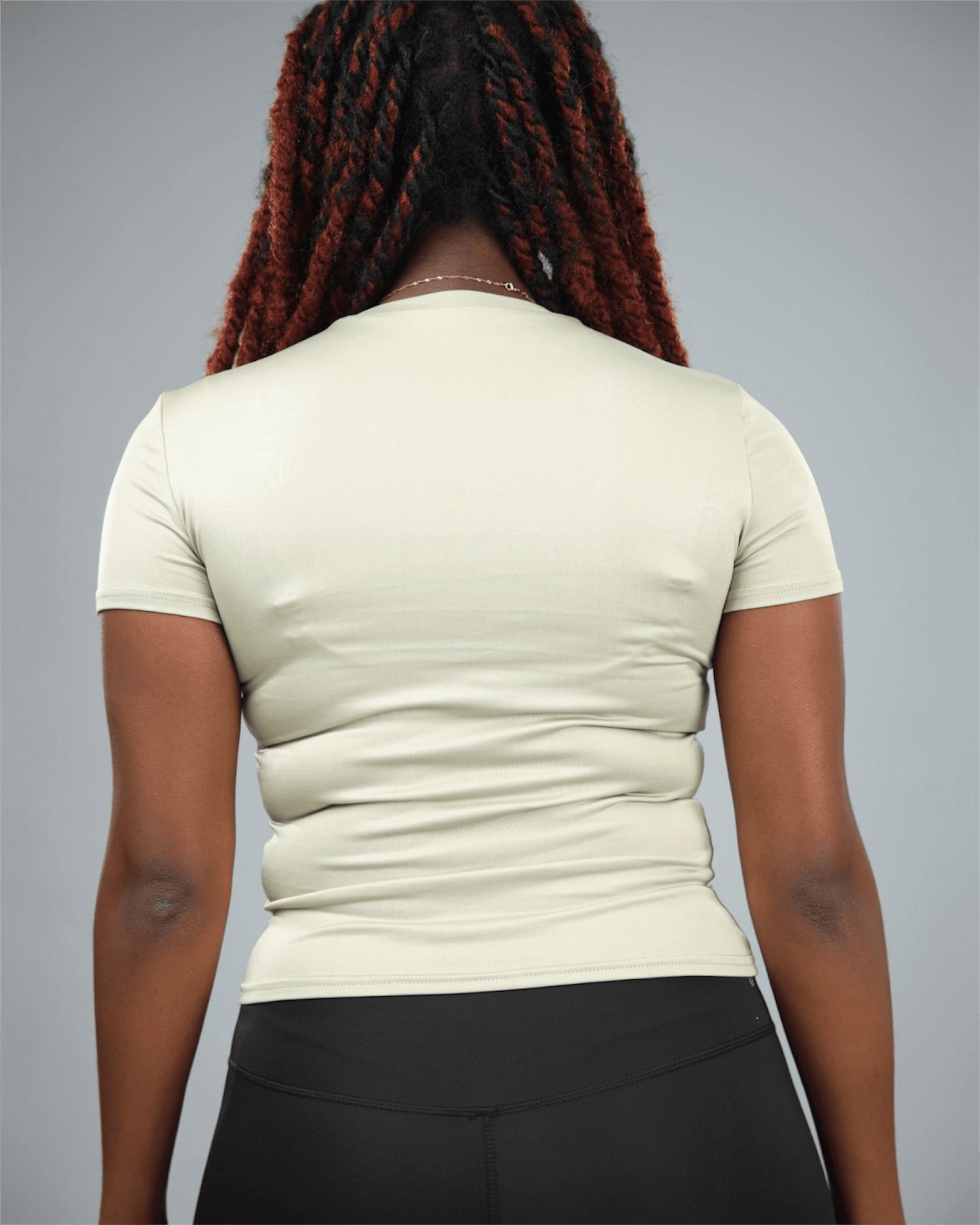 Woman wearing an olive green t-shirt and black leggings against a grey background back view