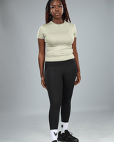 Person wearing a light green t-shirt and black leggings on a gray background
