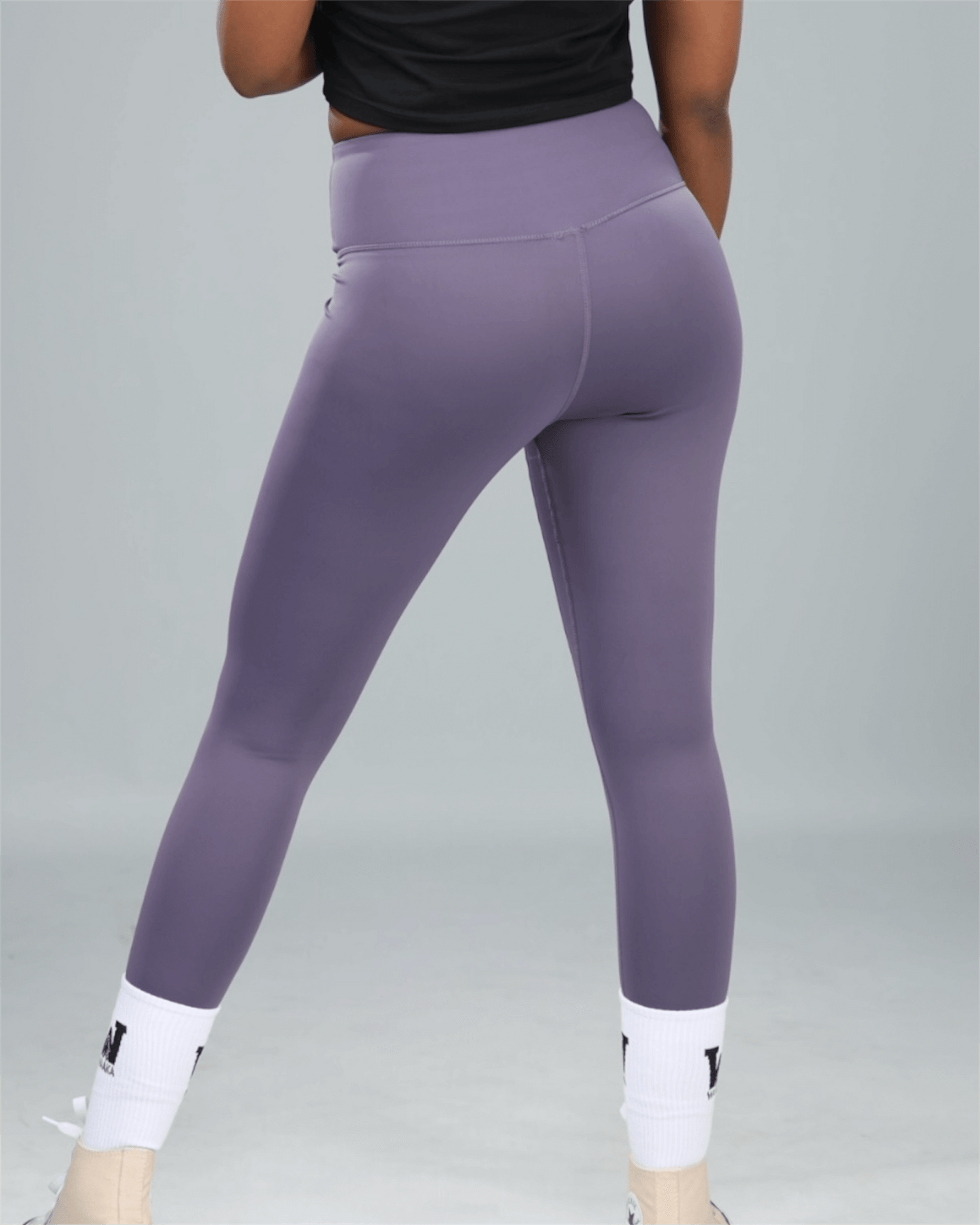 Purple leggings worn by a person on a gray background back view