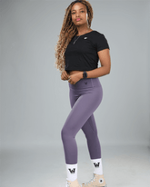 Woman wearing a black crop top and purple leggings on a gray background