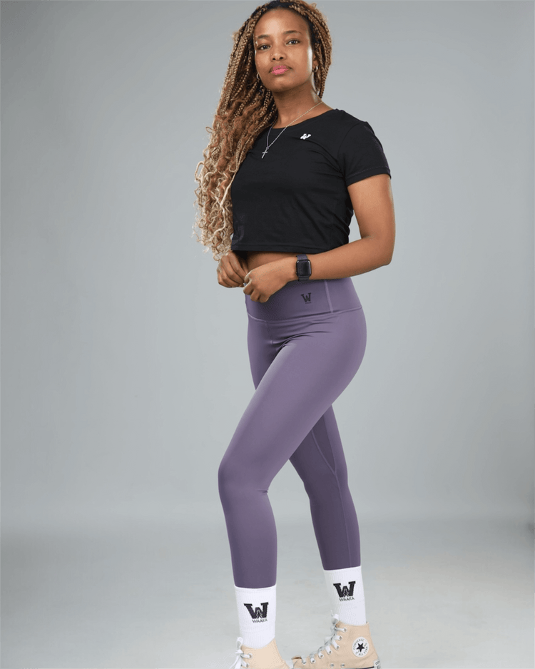 Woman wearing a black crop top and purple leggings on a gray background