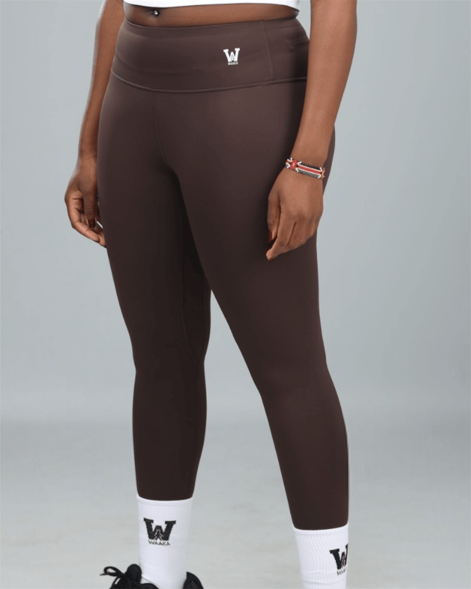 woman wearing brown gym leggings with waaka logo on a grey background