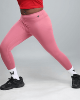 Person wearing pink leggings with a logo, black sneakers, and white socks on a gray background