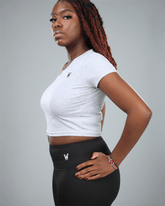 Woman wearing a light grey crop top and black leggings with logos on a gray background