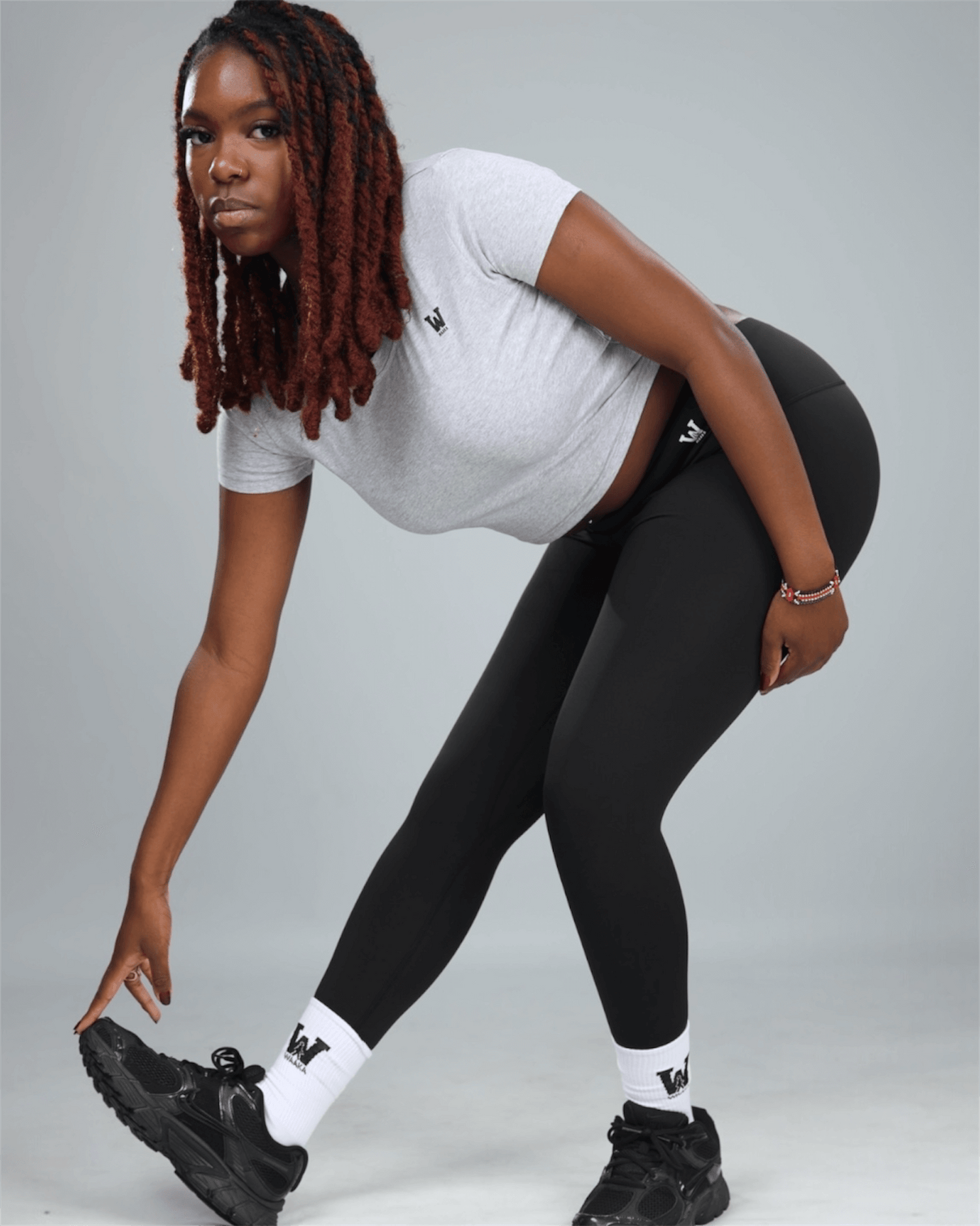 Person wearing a white t-shirt, black leggings, and black sneakers on a gray background