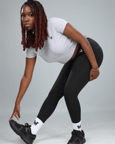 Person wearing a white t-shirt, black leggings, and black sneakers on a gray background