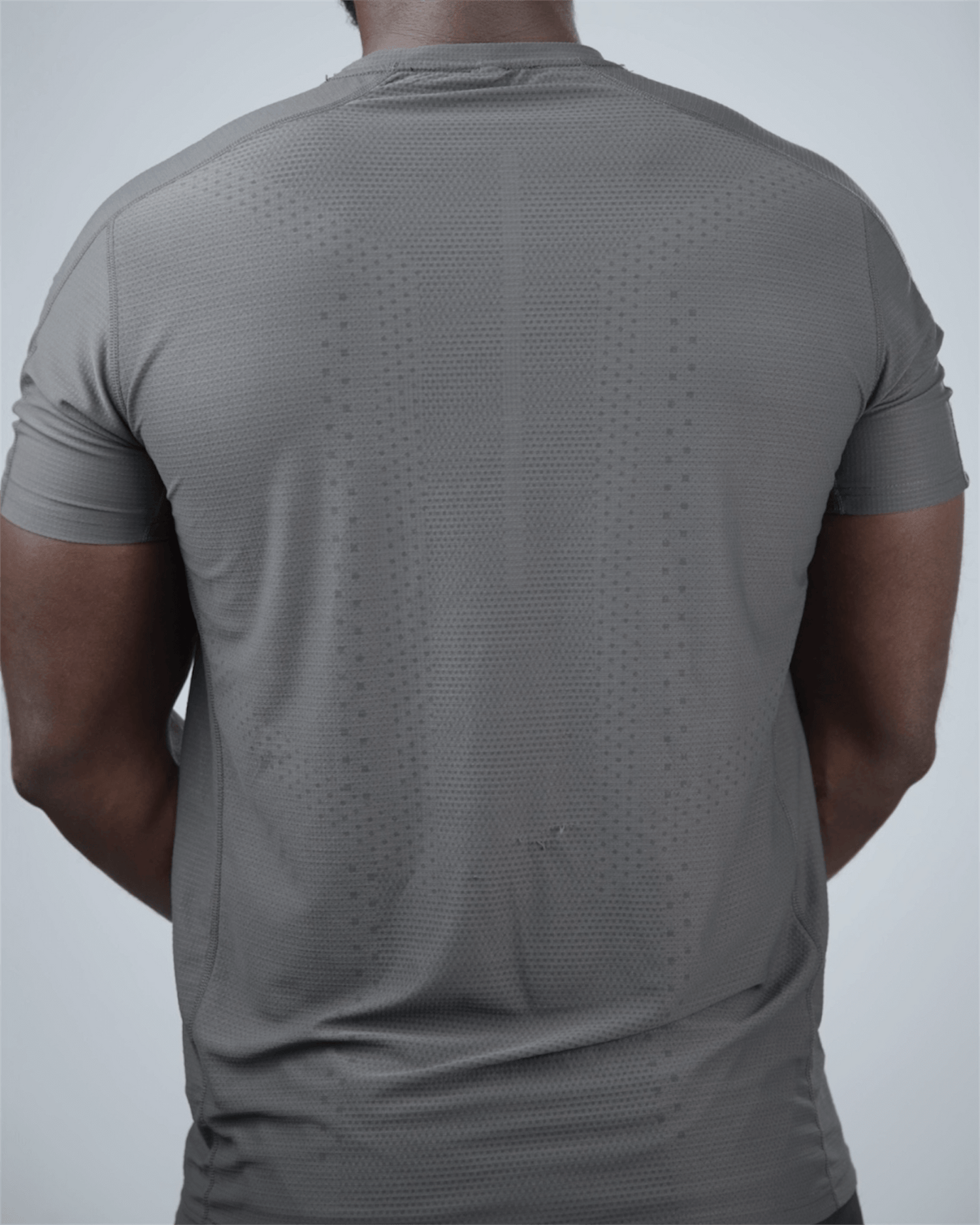Man wearing a grey patterned activewear t-shirt with waaka logo on a light grey background back view - Surge