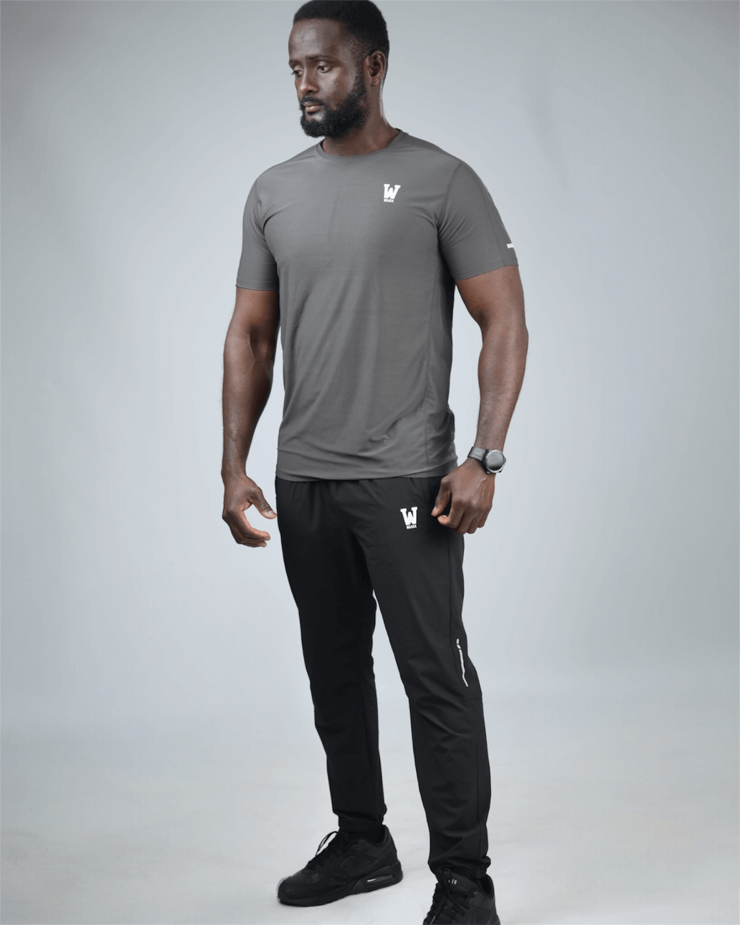Man wearing a gray t-shirt and black pants with waaka logos on a light gray background