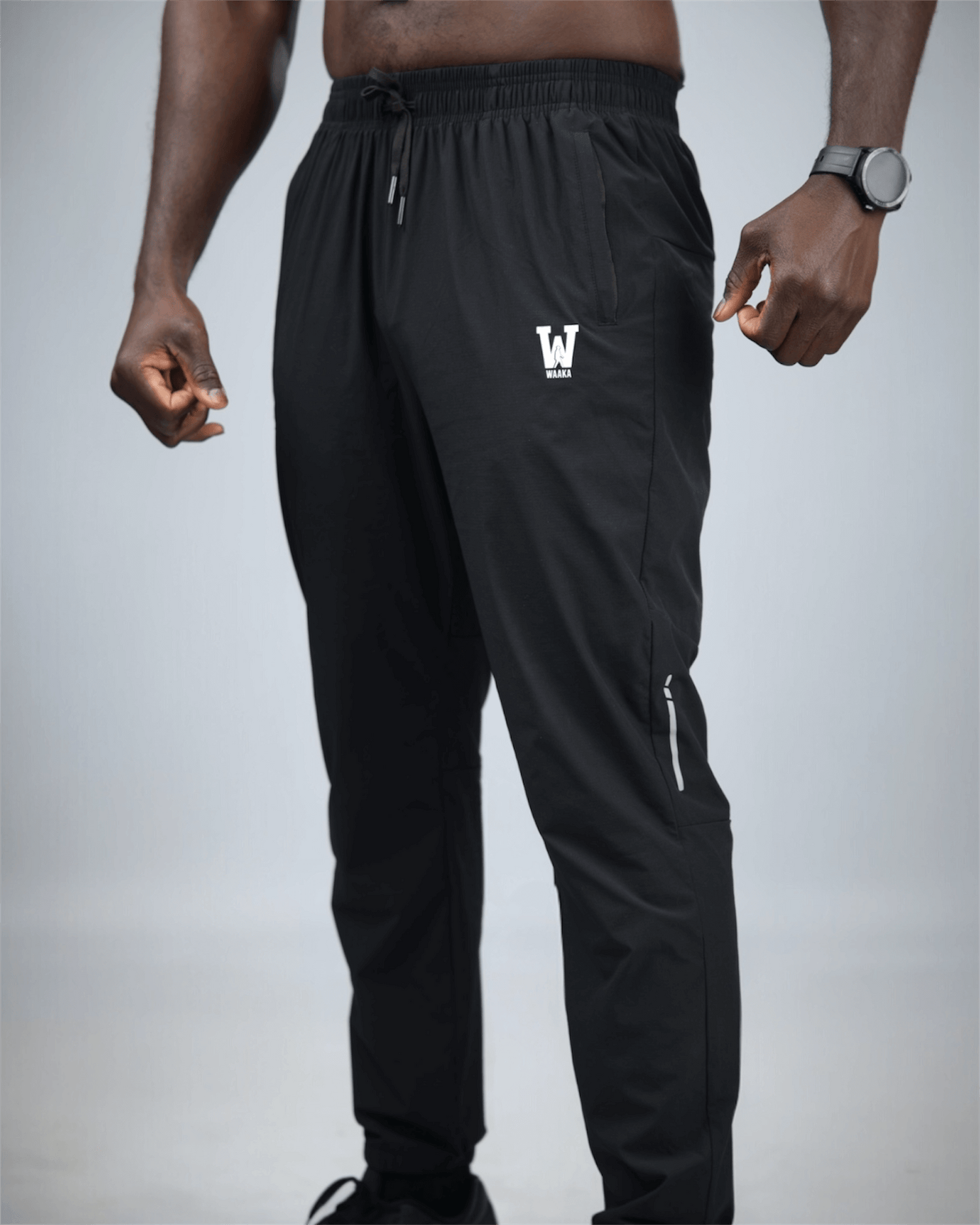 Black jogger pants with a logo on the leg worn by a person against a gray background
