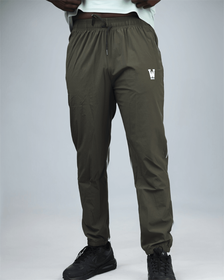 khaki green pants with waaka logo on a grey background front view. core performance pant