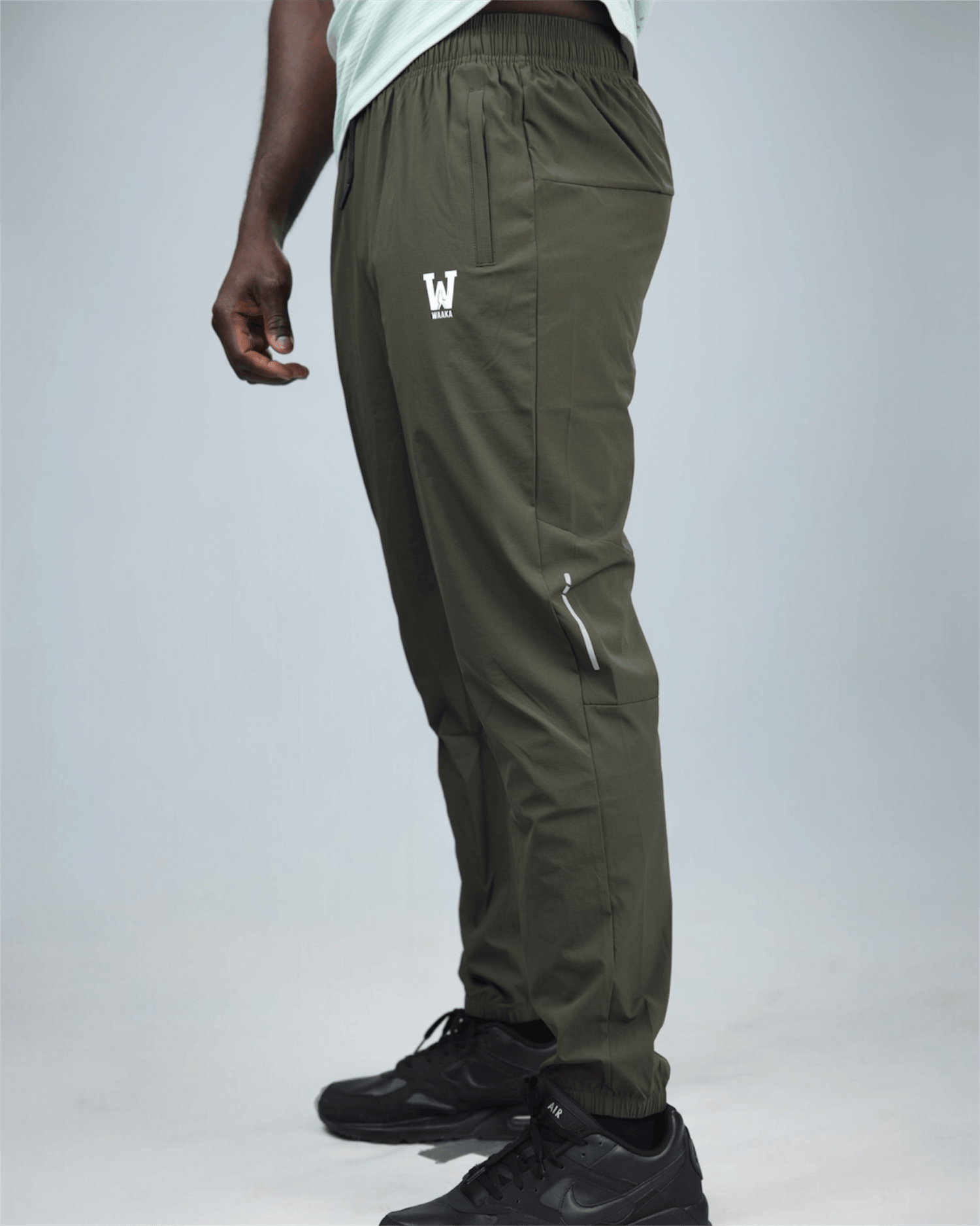 khaki green pants with waaka logo on a grey background side view. core performance pant