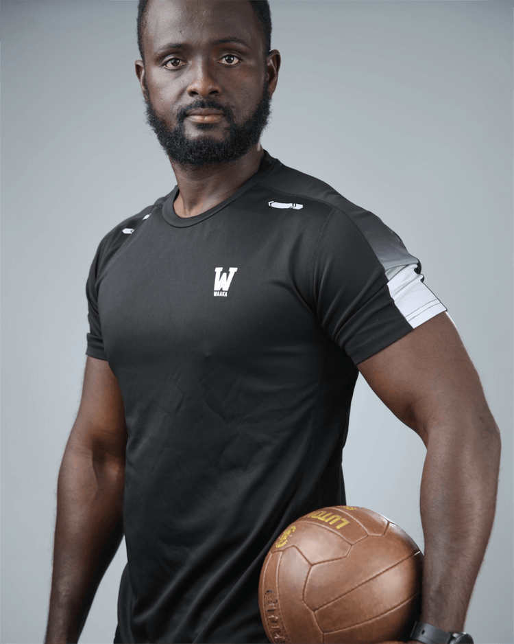 Man wearing eco training t-shirt black sports jersey holding a brown medicine ball against a gray background