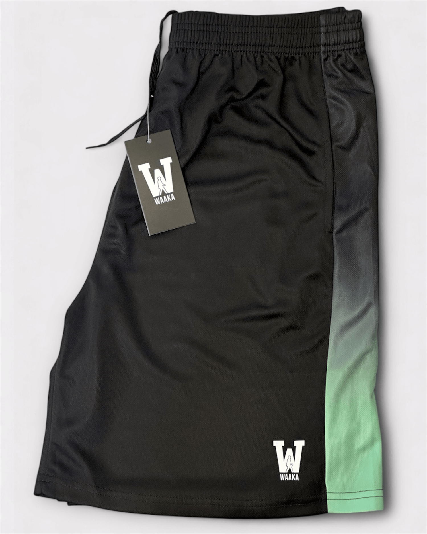 Black shorts with gradient design and Waaka tag on a light gray background