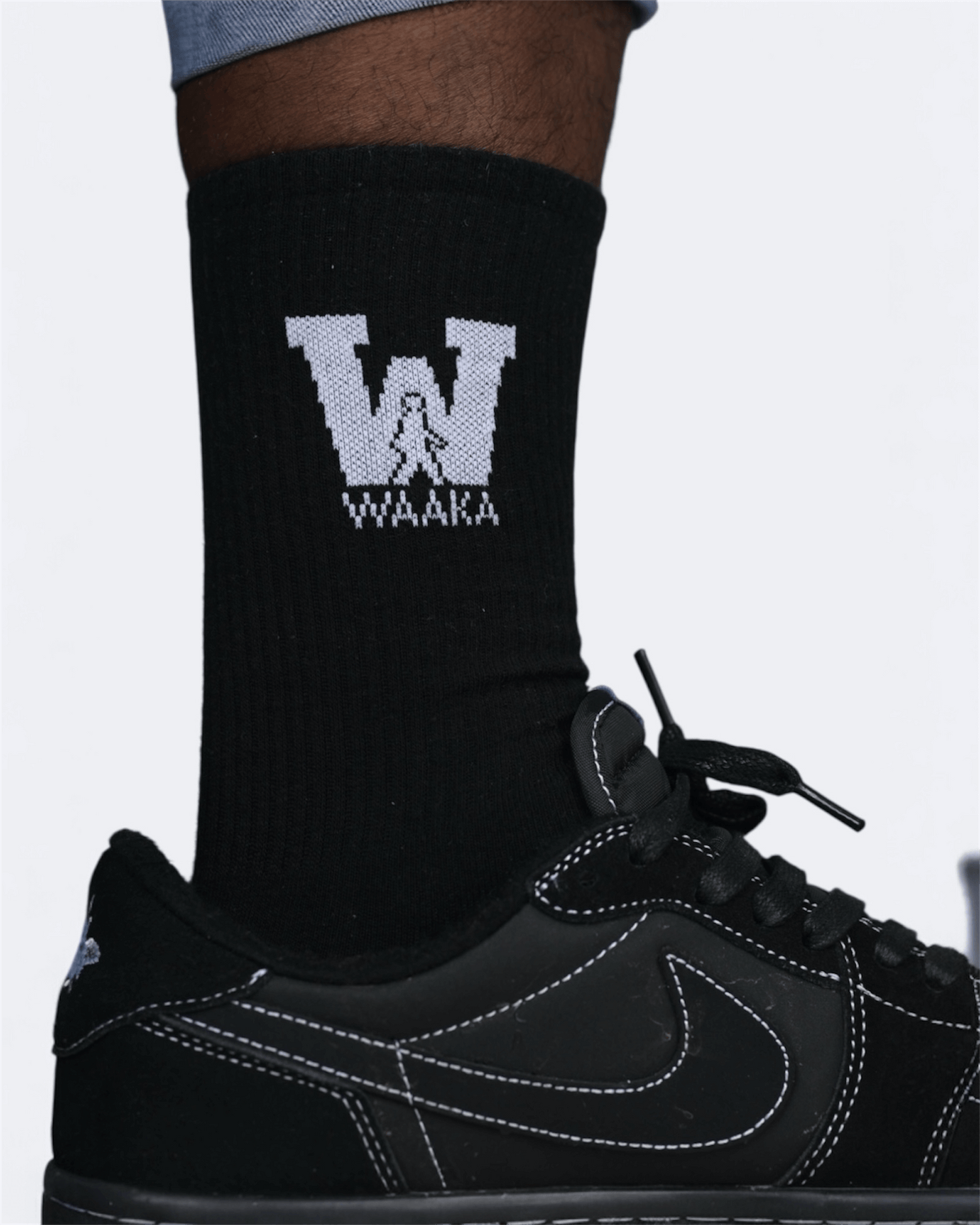 Black sock with a logo and text, worn with a black sneaker on a light gray background