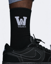 Black sock with a logo and text, worn with a black sneaker on a light gray background