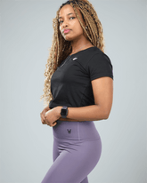 Woman wearing a black athletic shirt and purple leggings with a gray background