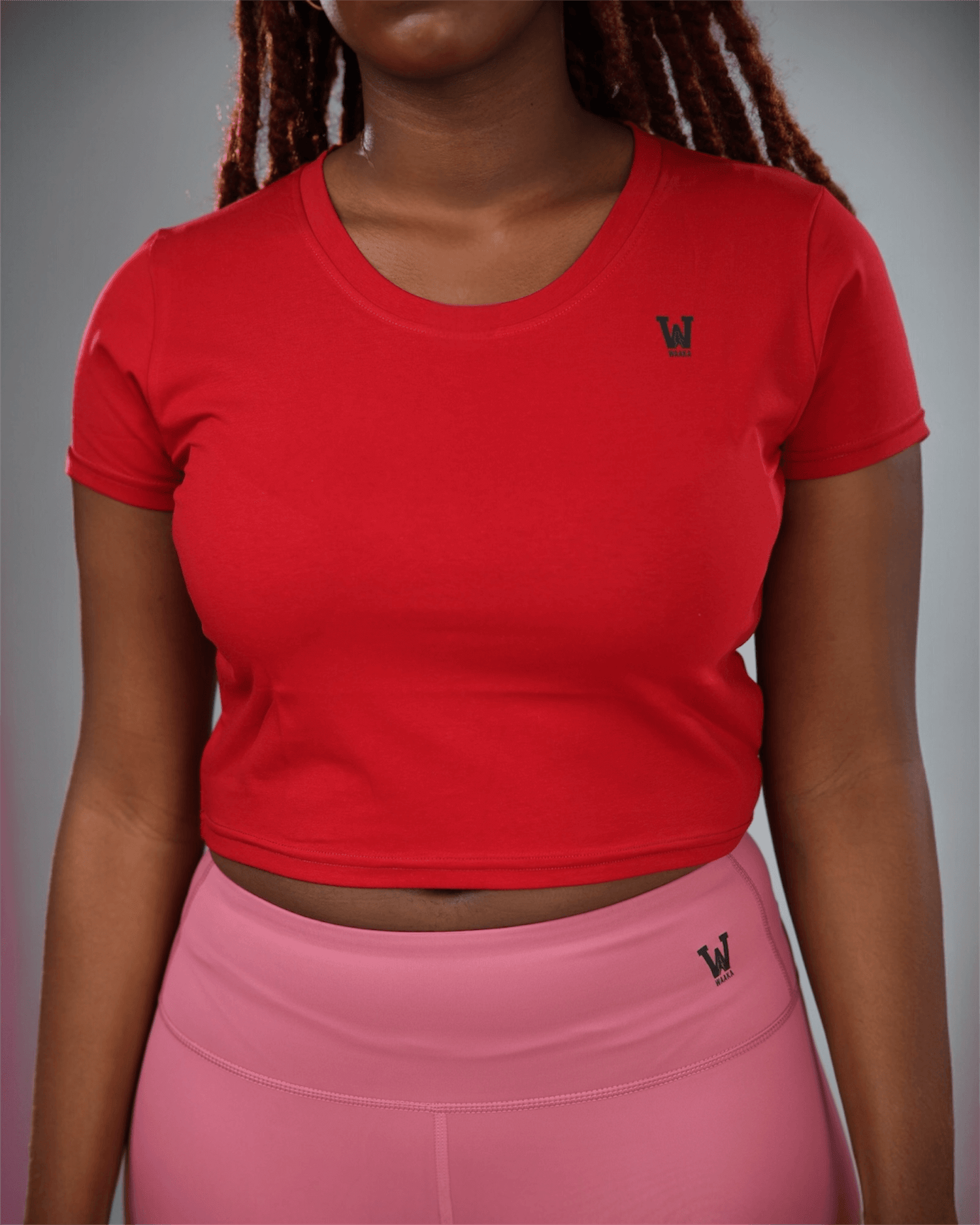 woman wearing a red crop top and pink leggings with waaka logo on a grey background