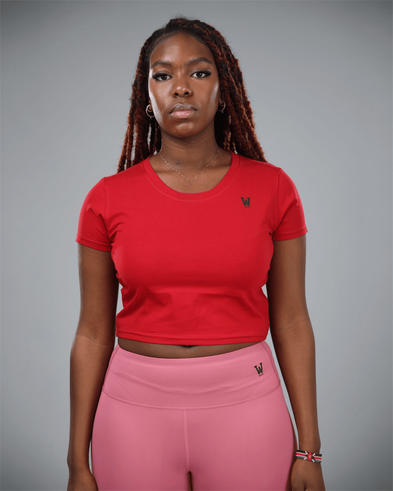 woman wearing a red crop top and pink leggings with waaka logo on a grey background front view