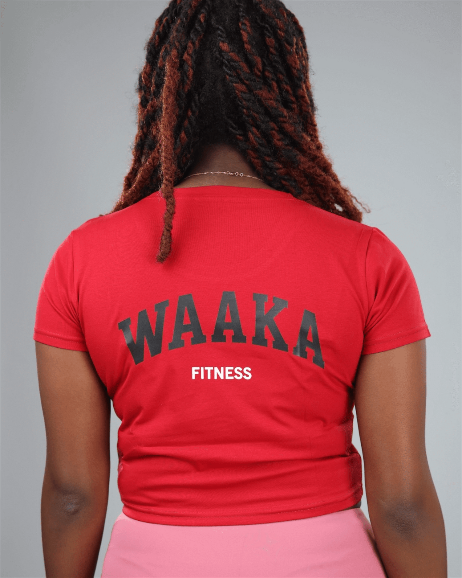 woman wearing a red crop top and pink leggings with waaka logo on a grey background back view