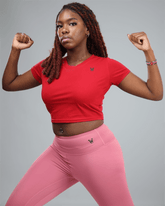 woman wearing a red crop top and pink leggings with waaka logo on a grey background flexing muscle