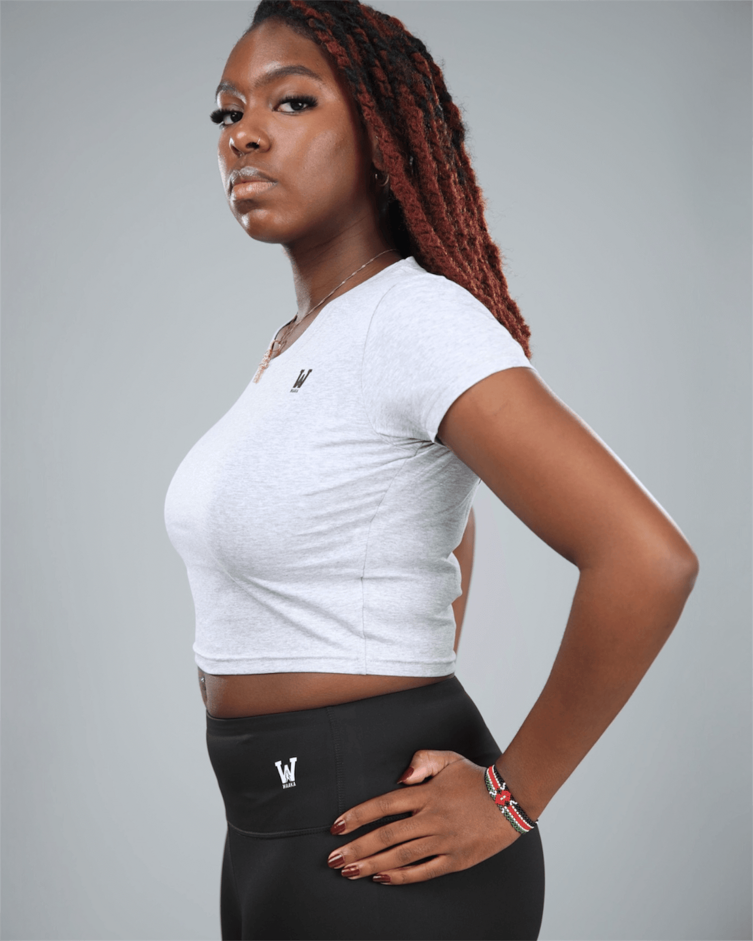 Woman wearing a grey Nova crop top and black leggings with logos on a gray background