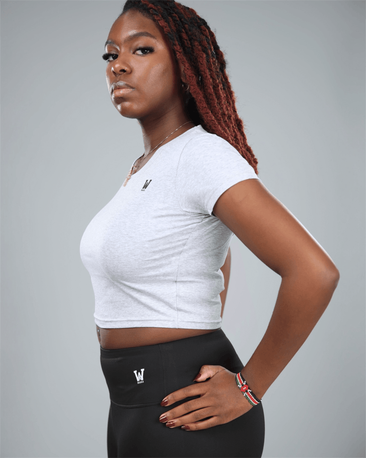 Woman wearing a grey Nova crop top and black leggings with logos on a gray background