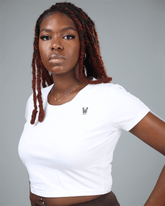 Woman wearing a white crop top and brown leggings with a gray background