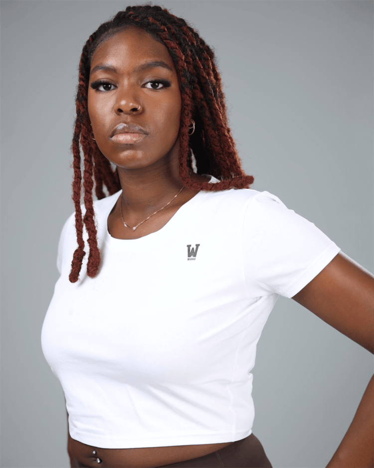 Woman wearing a white crop top and brown leggings with a gray background