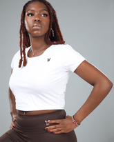 Woman wearing a white crop top and brown leggings with a gray background