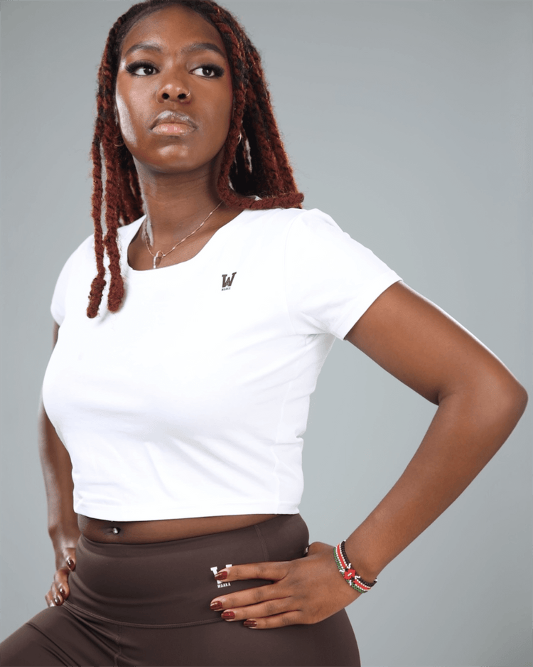 Woman wearing a white crop top and brown leggings with a gray background