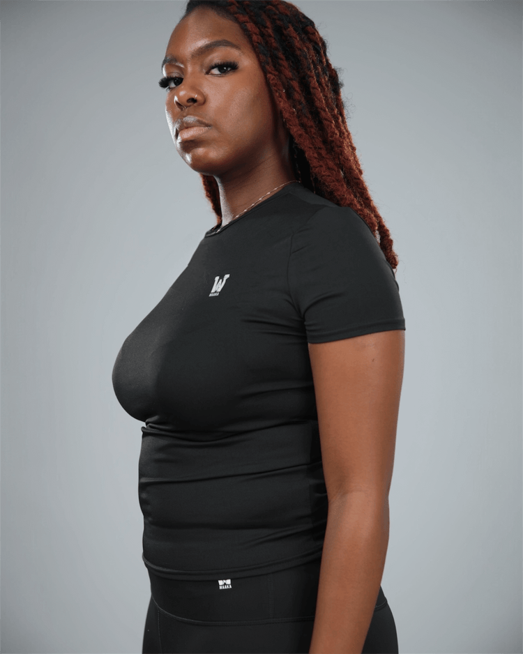 Woman wearing a black short sleeve  t-shirt with a logo on a grey background side view