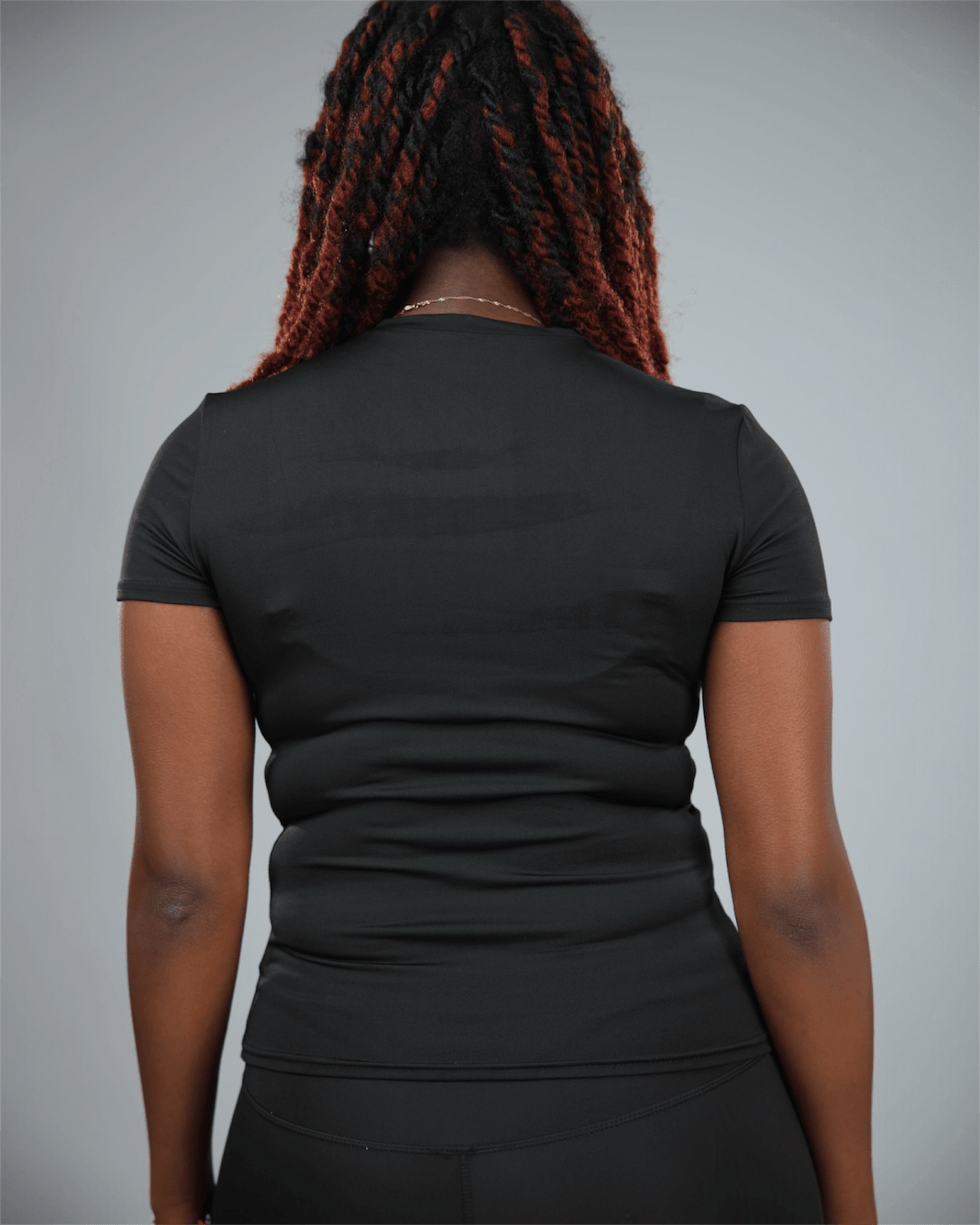 Woman wearing a black short sleeve  t-shirt with waaka logo on a grey background back view