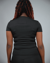 Woman wearing a black short sleeve  t-shirt with waaka logo on a grey background back view