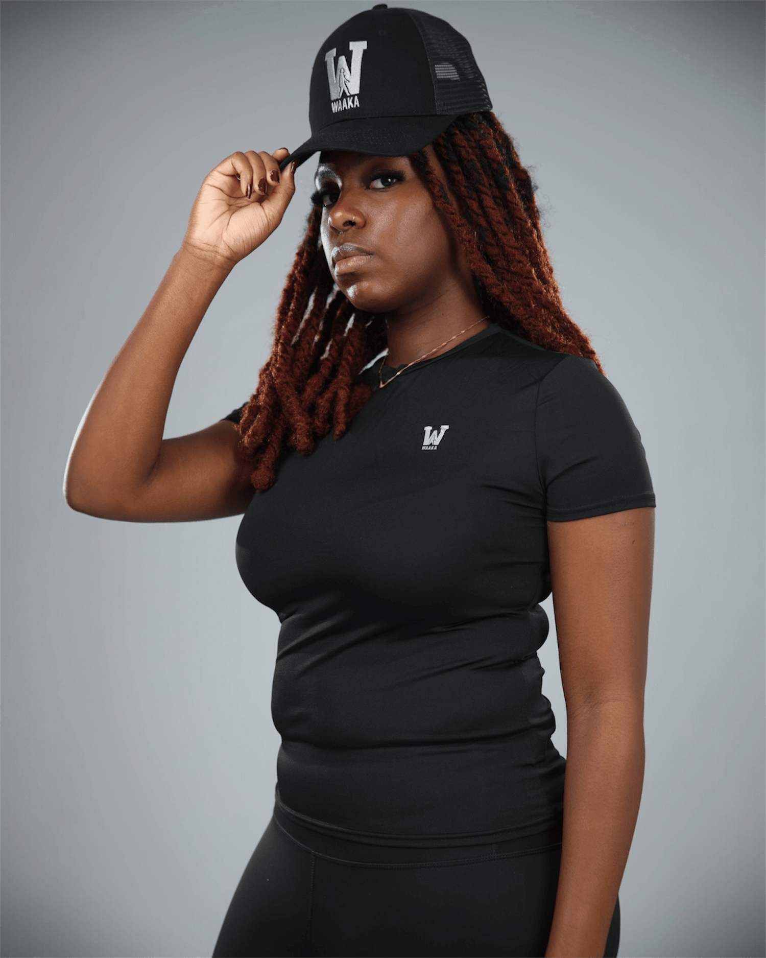 Woman wearing a black short sleeve  t-shirt with waaka logo on a grey background with a black cap