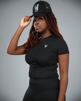Woman wearing a black short sleeve  t-shirt with waaka logo on a grey background with a black cap