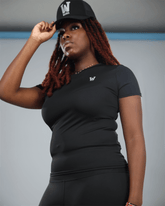 Woman wearing a black short sleeve fluxa t-shirt and cap with waaka logo on a grey background 